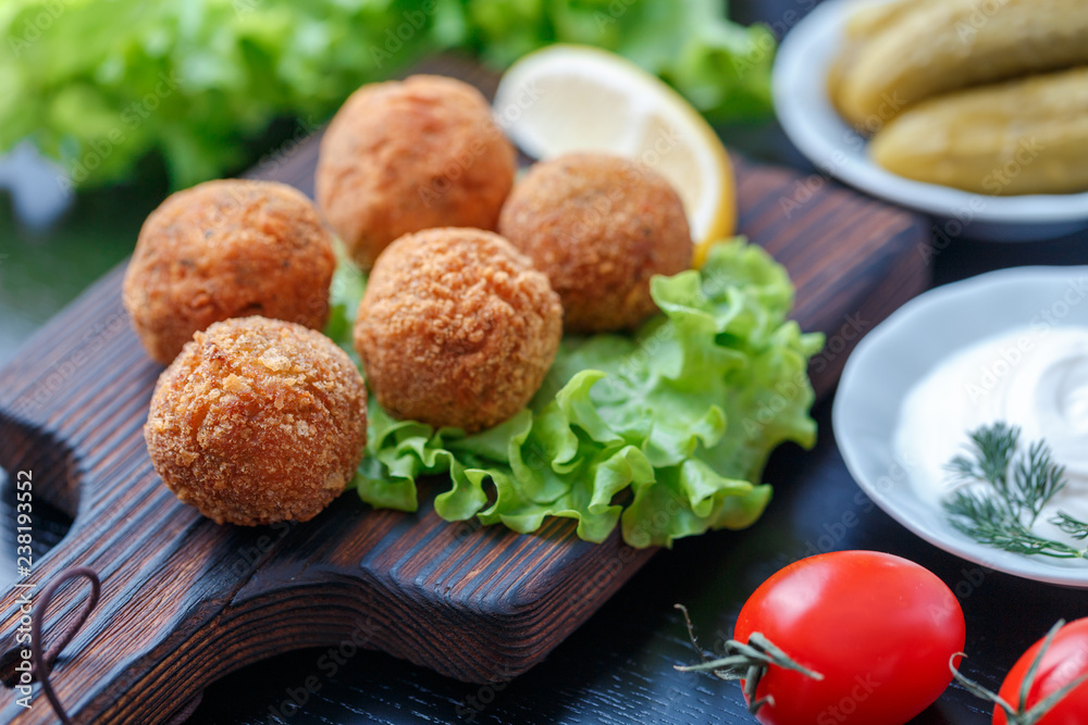 Falafel lies on a wooden cutting board. On the table lie tomatoes, cucumbers, lettuce, dill, lemon, sour cream. Falafel lies on a wooden cutting board. On the table lie tomatoes, cucumbers, lettuce, dill, lemon, sour cream.
