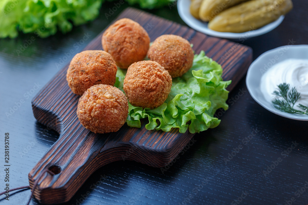 Falafel lies on a wooden cutting board. On the table lie tomatoes, cucumbers, lettuce, dill, lemon, sour cream. Falafel lies on a wooden cutting board. On the table lie tomatoes, cucumbers, lettuce, dill, lemon, sour cream.