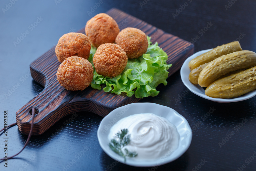 Falafel lies on a wooden cutting board. On the table lie tomatoes, cucumbers, lettuce, salad, dill, lemon, sour cream. Falafel lies on a wooden cutting board. On the table lie tomatoes, cucumbers, lettuce, salad, dill, lemon, sour cream.