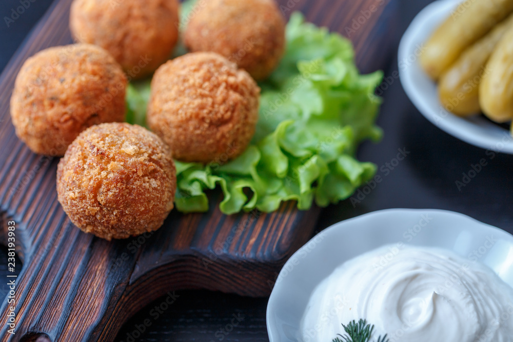 Falafel lies on a wooden cutting board. On the table lie tomatoes, cucumbers, lettuce, salad, dill, lemon, sour cream. Falafel lies on a wooden cutting board. On the table lie tomatoes, cucumbers, lettuce, salad, dill, lemon, sour cream.
