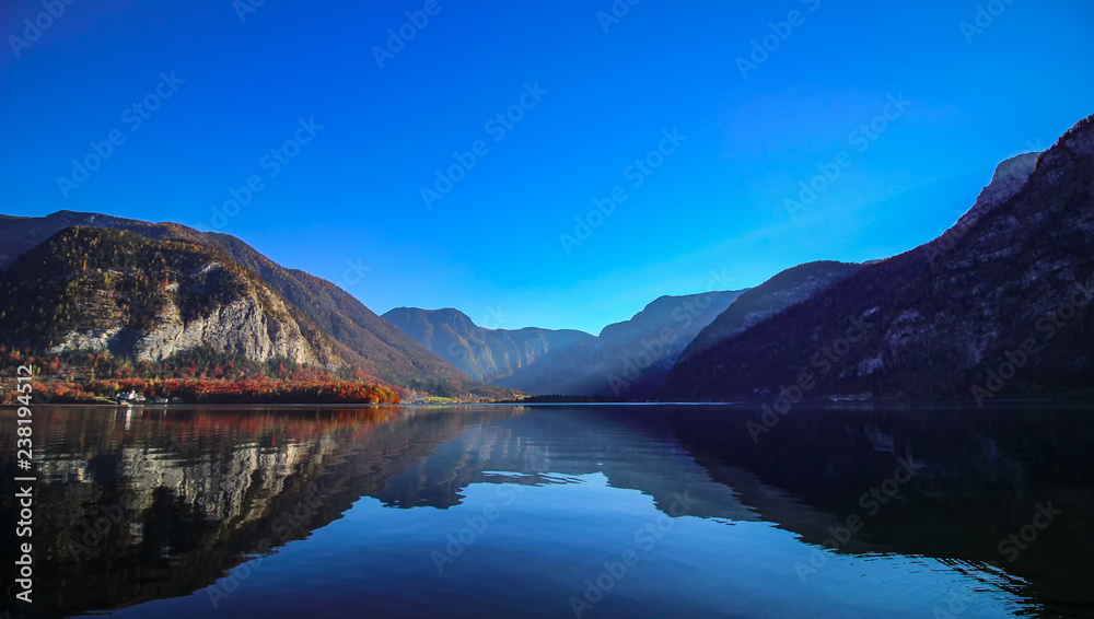 Beautiful fall morning view on Hallstatt lake with blue sky, historic church and mountains with sunrays