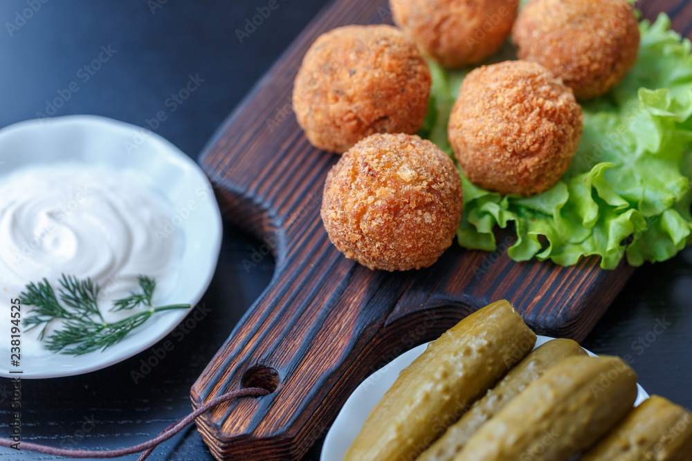 Falafel lies on a wooden cutting board. On the table lie tomatoes, cucumbers, lettuce, salad, dill, lemon, sour cream. Falafel lies on a wooden cutting board. On the table lie tomatoes, cucumbers, lettuce, salad, dill, lemon, sour cream.