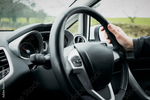 A womans hand holding a steering wheel of a car while driving.