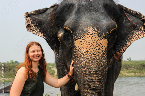 Happy smiling girl traveler with red hair in a green t-shirt holding a big elephant by the trunk photo