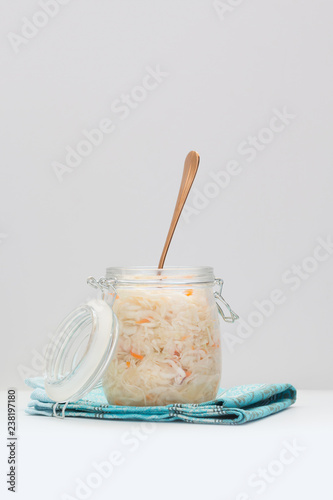 Homemade sauerkraut, marinated cabbage salad in a glass jar with a fork on a white table.  Fermented healthy vegetarian food concept. Copy space.