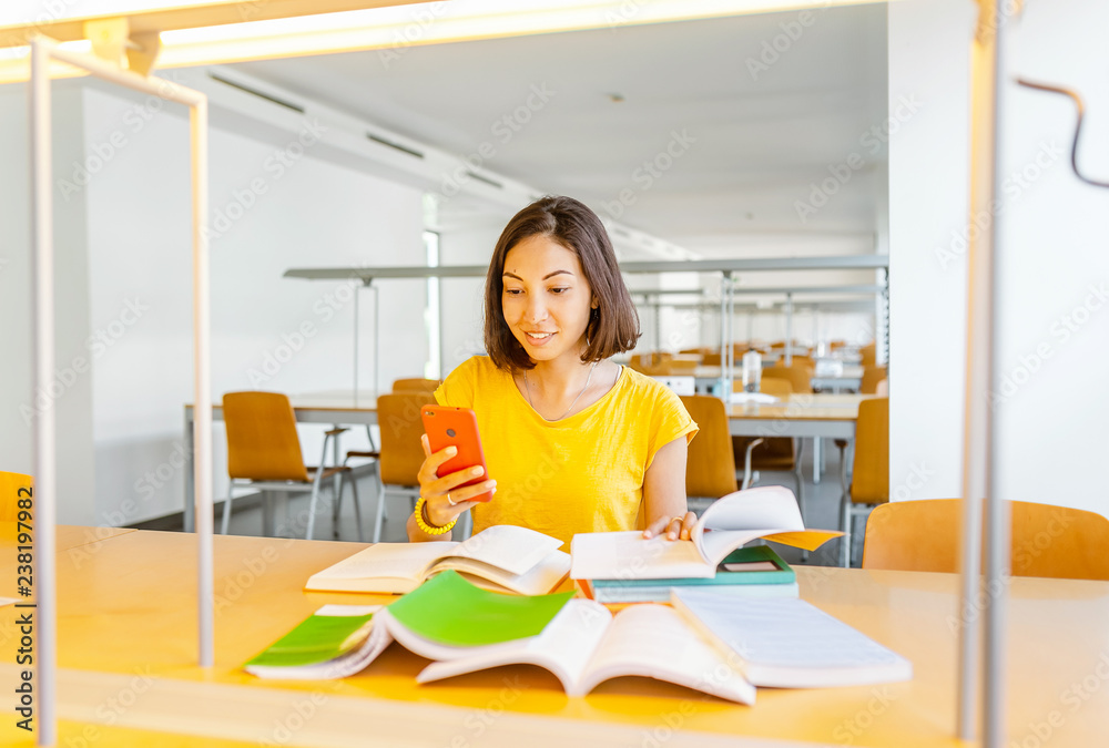 Woman student with smartphone and pile of books in university library