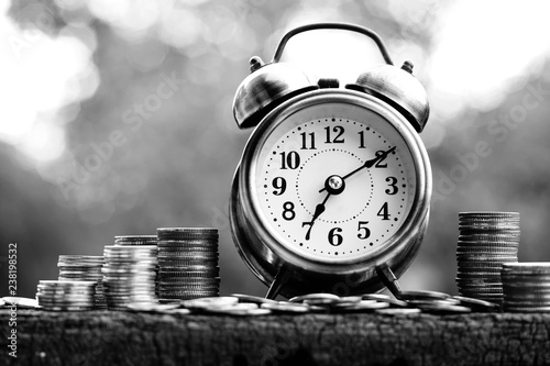 Alarm clock and coin stacks on wooden table with blur green garden background, bright morning color tone, finance and business concept