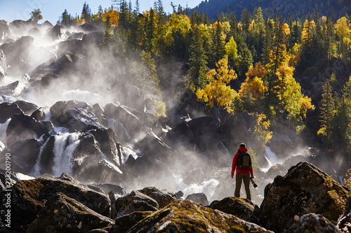 Photographer with backpack enjoying amazing waterfall Travel Lifestyle and success concept vacations into the wild nature