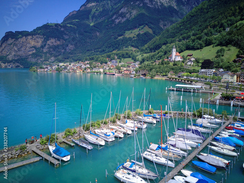 Aerial view of sail boats & yachts parking in a marina on Lake Lucerne in Fluelen, Switzerland, with majestic alpine mountains and a beautiful lakeside village in background on a sunny summer day photo