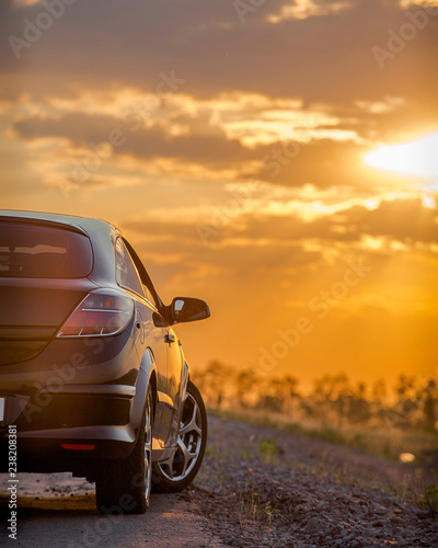 beautiful black modern car stands on asphalt road in summer illuminated by the rays of the sunset © Ambartsumian