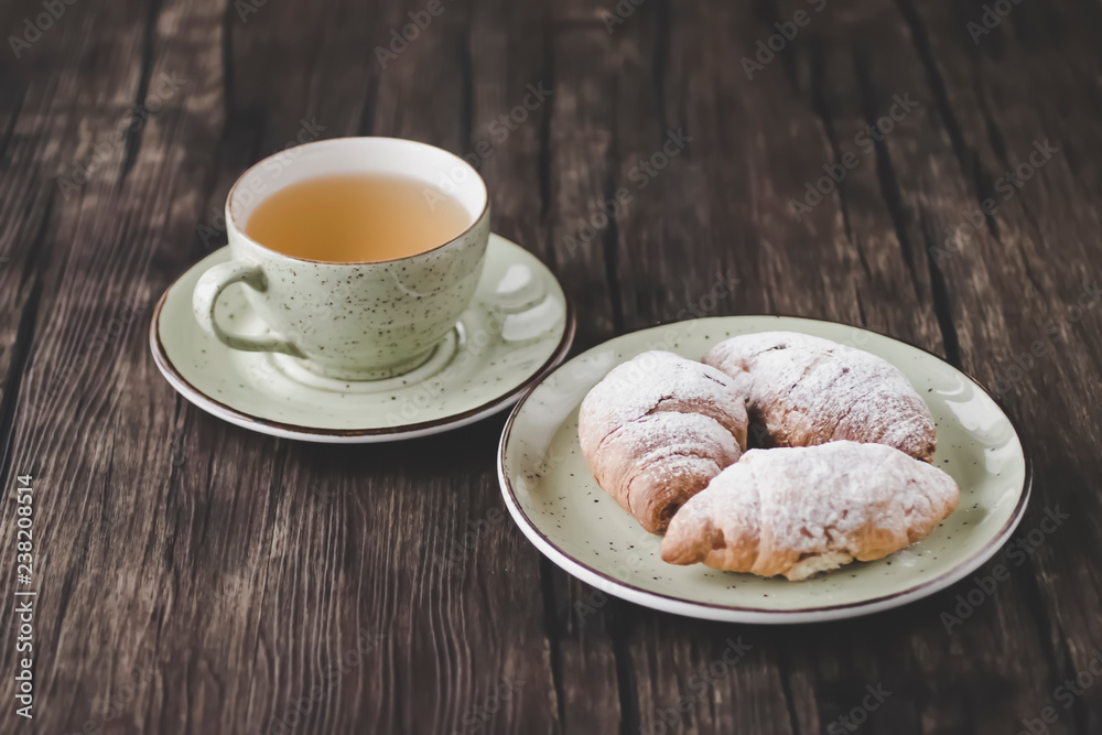 Freshly baked croissants cup with green tea on a brown wooden background. Freshly baked croissants cup with green tea on a brown wooden background.
