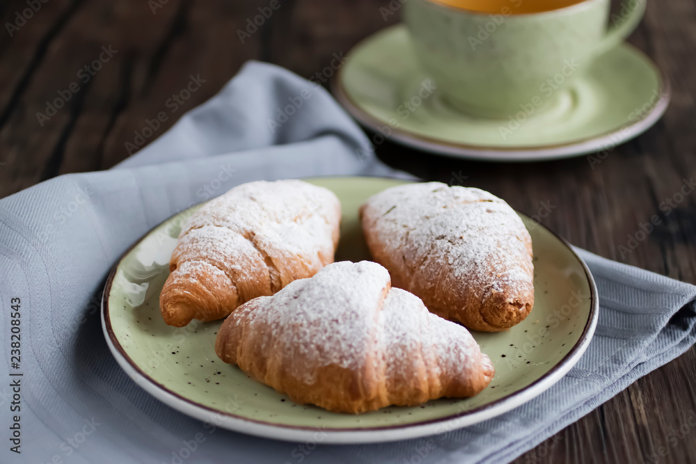 Freshly baked croissants cup with green tea on a brown wooden background.