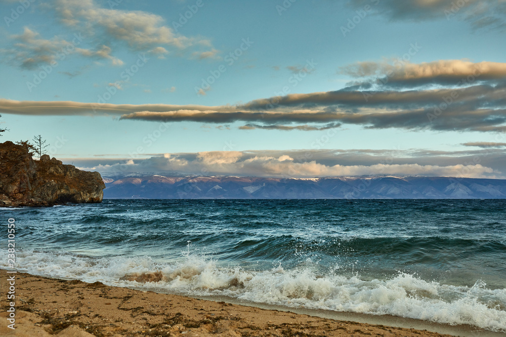 Azure beach with stony mountains and clear water of Baikal on a cloudy day.