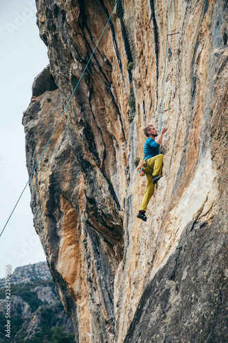 man in yellow pants and blue t-shirt climbs a rock top rope