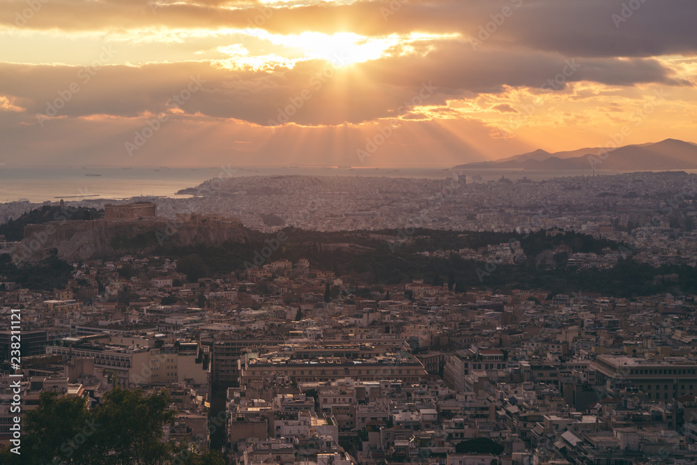 Fototapeta premium Beautiful sunset above Athens city and acropolis with sun rays light throw the clouds