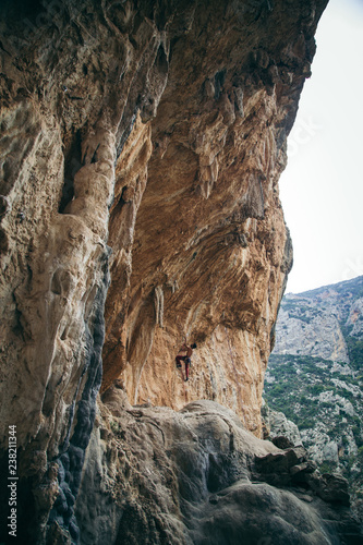 man climbs an overhang tufa cliff like a cave in Greece