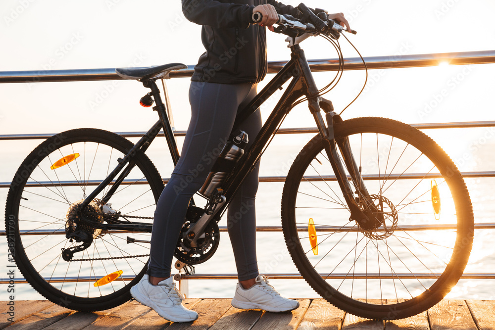 Photo of sportive woman standing with bicycle on boardwalk, during sunrise over sea Photo of sportive woman standing with bicycle on boardwalk, during sunrise over sea