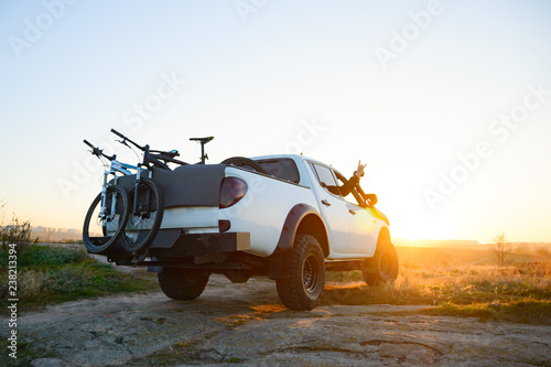 Friends Driving Pickup Offroad Truck in the Mountains with Bikes in the Body at Sunset. Adventure and Travel Concept.