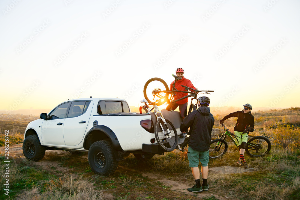 Friends Taking MTB Bikes off the Pickup Offroad Truck in Mountains at Sunset. Adventure and Travel Concept. - obrazy, fototapety, plakaty 