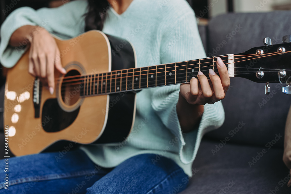 cropped image of mixed race girl in turquoise sweater playing acoustic guitar on sofa at home