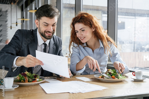 Businesspeople having business lunch at restaurant sitting eating man showing woman document conditions happy