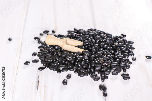 Lot of whole raw black turtle beans with wooden scoop on white wood