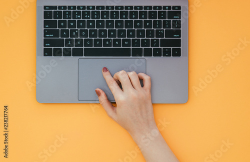 Φωτογραφία Female hand uses a touchpad on a laptop on a yellow background