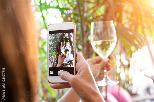 Woman taking photo of white wine on her smartphone in restaurant.