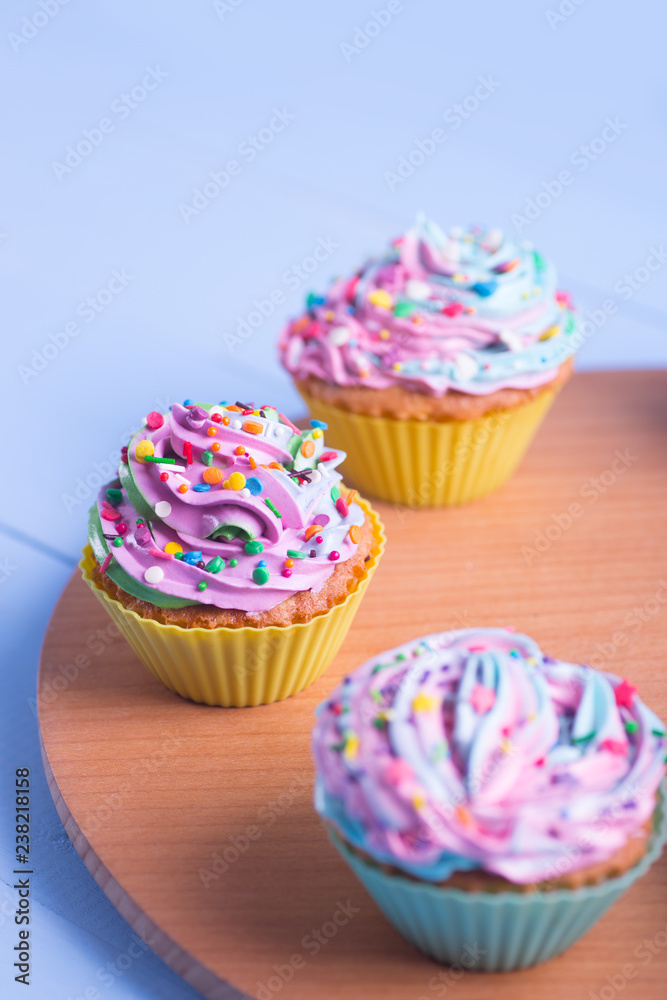 Closeup different colorful cupcakes decorated with sprinkles on wooden round desk.