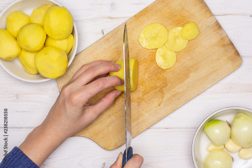 Woman hands are cutting potatoes. recipe step by step baked potatoes with onion on chopping board flatlay on white wood Woman hands are cutting potatoes. recipe step by step baked potatoes with onion on chopping board flatlay on white wood