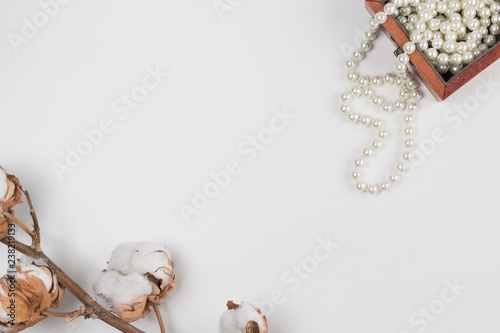 Pearl necklace in wooden box and branch of dried cotton flower on white background. Copy space, top view, close-up