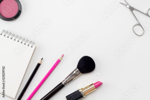 Workspace with notebook, black and pink pencils, lipstick, blusher, make-up brush and scissors on the white background. Fashion woman concept. Flat lay, top view, copy space, mock up, layout design