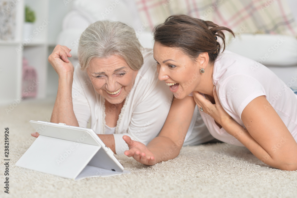 Portrait of mother and her adult daughter lying on floor and looking at tablet Portrait of mother and her adult daughter lying on floor and looking at tablet