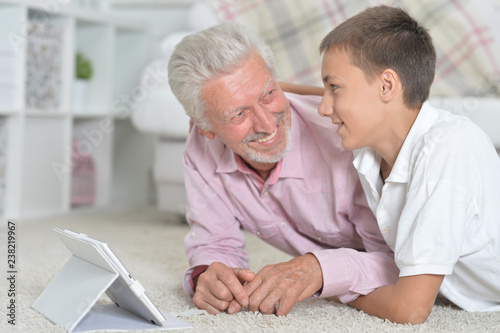 Grandfather with grandson using laptop while lying on floor 