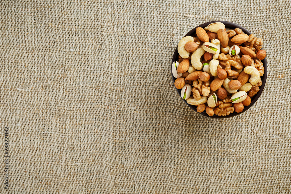 Mix of different nuts in a wooden cup against the background of fabric from burlap. Nuts as structure and background, macro. Top view. Mix of different nuts in a wooden cup against the background of fabric from burlap. Nuts as structure and background, macro. Top view.