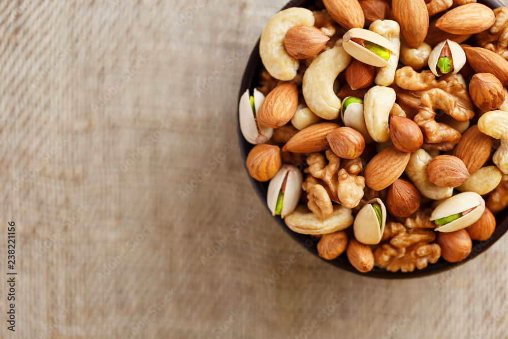 Mix of different nuts in a wooden cup against the background of fabric from burlap. Nuts as structure and background, macro. Top view. Mix of different nuts in a wooden cup against the background of fabric from burlap. Nuts as structure and background, macro. Top view.
