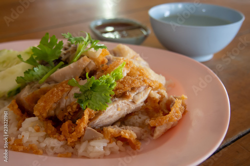 Close up Fried-Chicken Rice  in a plate and sprinkle with coriander. With chicken broth And a cup of dipping sauce on a wooden table.