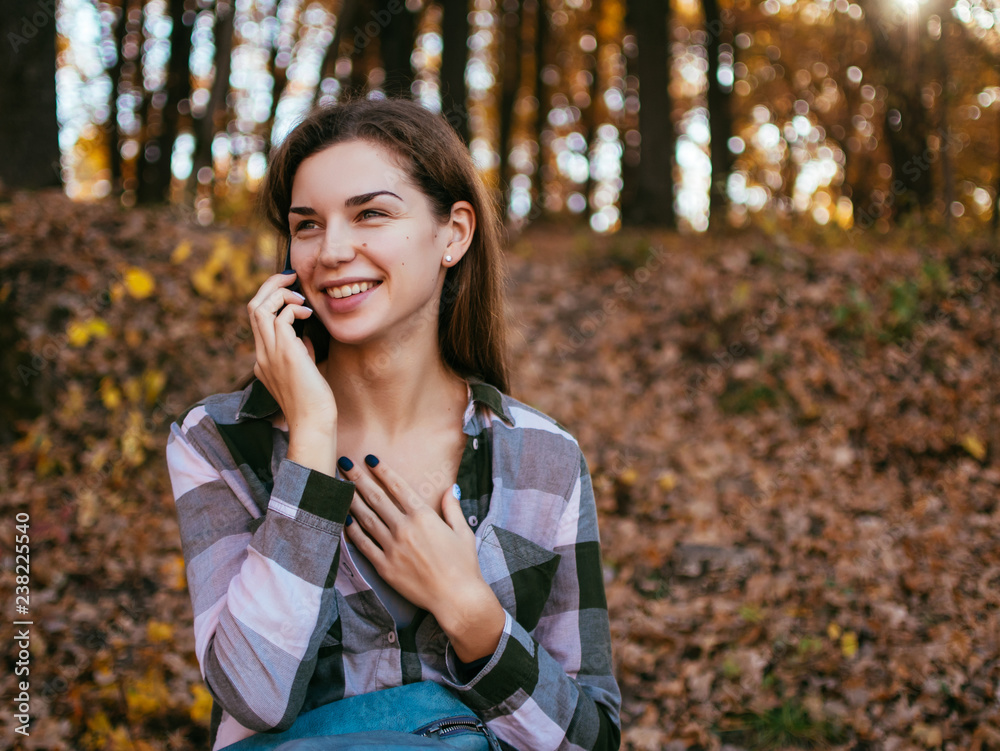 Young caucasian girl talking on a mobile phone on the background of the autumn forest Young caucasian girl talking on a mobile phone on the background of the autumn forest
