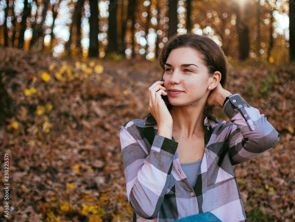 Young caucasian girl talking on a mobile phone on the background of the autumn forest Young caucasian girl talking on a mobile phone on the background of the autumn forest