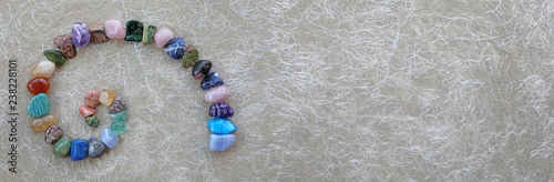 Crystal Fibonacci Spiral Background Banner -  carefully arranged crystal healing gemstones in spiral shape on left against rustic buff coloured fibre paper with copy space on right 
