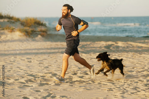 Canvas Print Happy bearded man running outdoor near sea with his dog