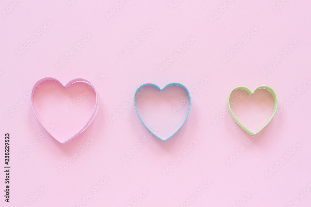 3 colorful cutters cookies in heart shape on pastel pink background. Concept Valentine's card. Top view Copy space for text.