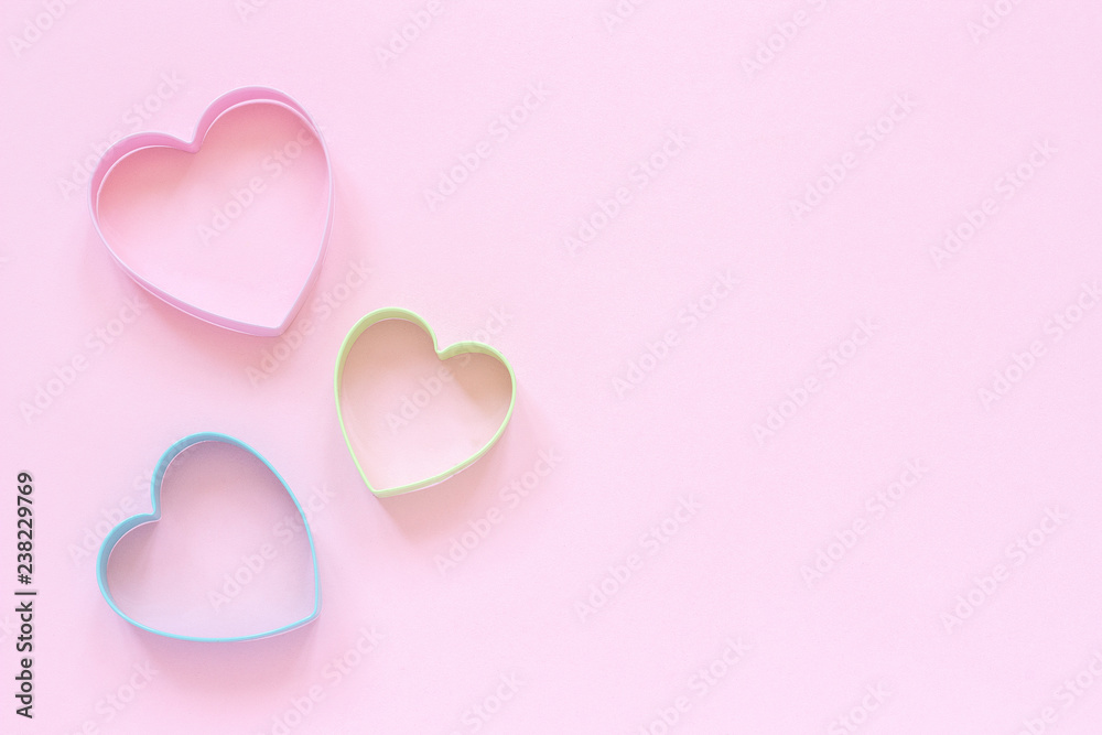 3 colored cutters cookies in heart shape on pastel pink background. Concept Valentine's card. Top view Copy space for text.