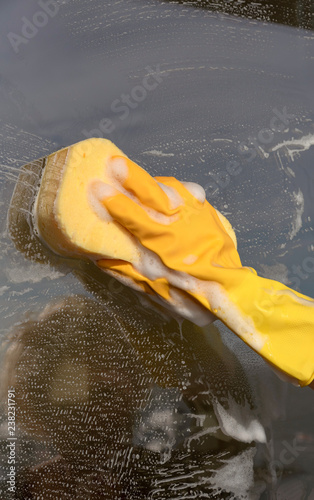 Hand wearing a yellow rubber glove and sponge cleaning a window.