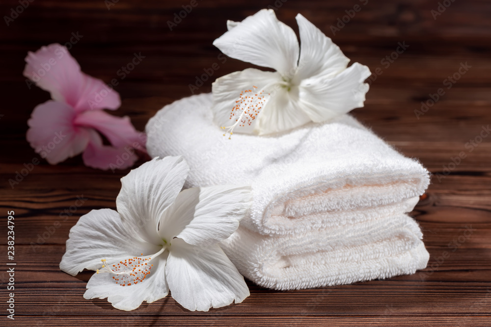 spa composition of white cotton towels folded and flowers of hibiscus on wooden table, close up spa composition of white cotton towels folded and flowers of hibiscus on wooden table, close up