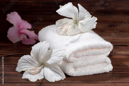 spa composition of white cotton towels folded and flowers of hibiscus on wooden table, close up