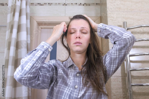 Sleepy woken woman combs her hair standing in front of a mirror in the bathroom. photo