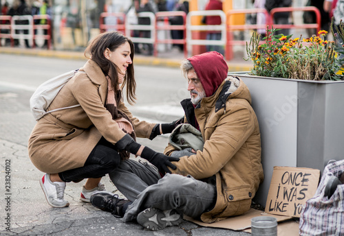 Young woman giving money to homeless beggar man sitting in city. photo