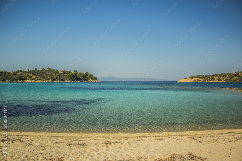 Aegean sand sea shore line Greece beach in summer clear hot weather time, colorful environment landscape of vivid blue water and opposite islands 