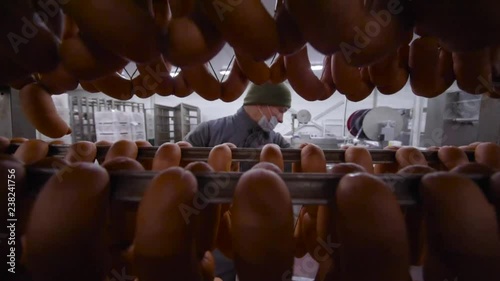 an employee of the meat factory carries a huge shelf of sausages on the background of the meat processing plant
